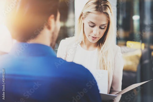 Two coworkers discussing business strategy in modern office.Successful confident hispanic businessman talking with blonde woman. Horizontal, blurred background.Flares.