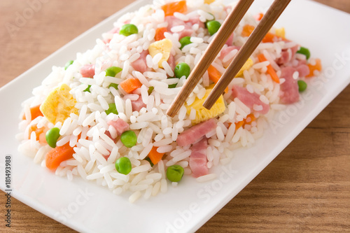 Chinese fried rice with vegetables and omelette on wooden table.