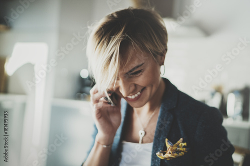 Attractive businesswoman talking with partner via modern telephone while writing some information in note book while sitting at living room in hotel.Blurred background.