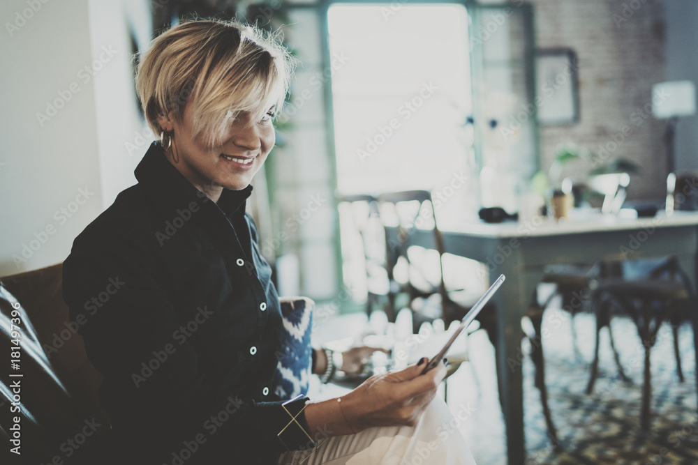 Smiling young woman wearing casual clothes and using electronic device while spending relax time home livingroom.Attractive woman owner communicating on digital tablet.Blurred background. Smiling young woman wearing casual clothes and using electronic device while spending relax time home livingroom.Attractive woman owner communicating on digital tablet.Blurred background.
