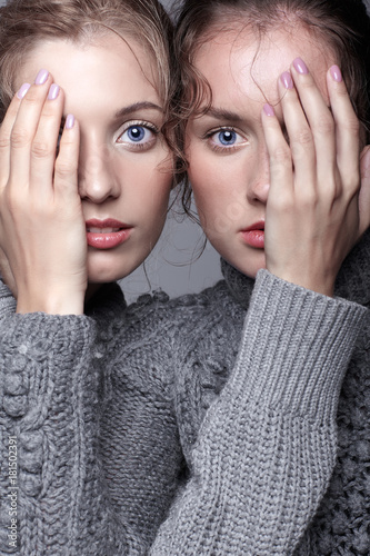 Two young women in gray sweaters on grey background. Beautiful girls stretching hands forward in embrace. Female friendship concept