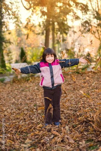 litle girl 6 years old throwing leaves in the air while laughing in a park