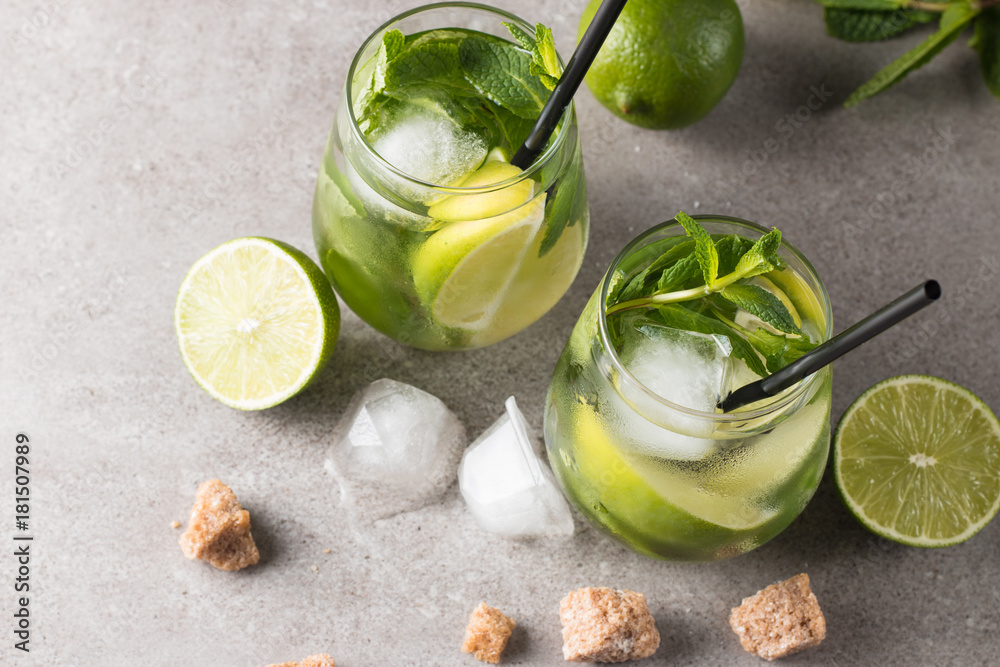 Fresh made mojito cocktail with lime, brown sugar, ice cubes and mint on a grey stone background. Alcoholic drink and lemonade concept. Fresh made mojito cocktail with lime, brown sugar, ice cubes and mint on a grey stone background. Alcoholic drink and lemonade concept.