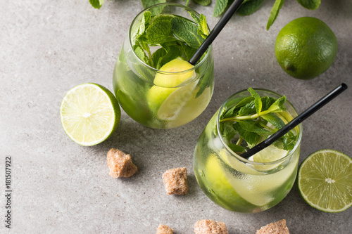 Fresh made mojito cocktail with lime, brown sugar, ice cubes and mint on a grey stone background. Alcoholic drink and lemonade concept.