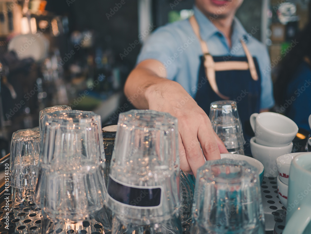 Handsome barista in blue apron uniform checking coffee glass cup at coffee shop cafe.