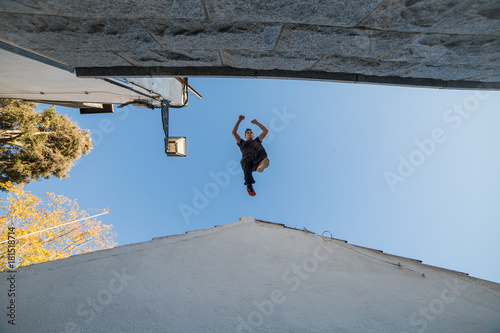 Young man doing impressive parkour jump from one roof to another. 