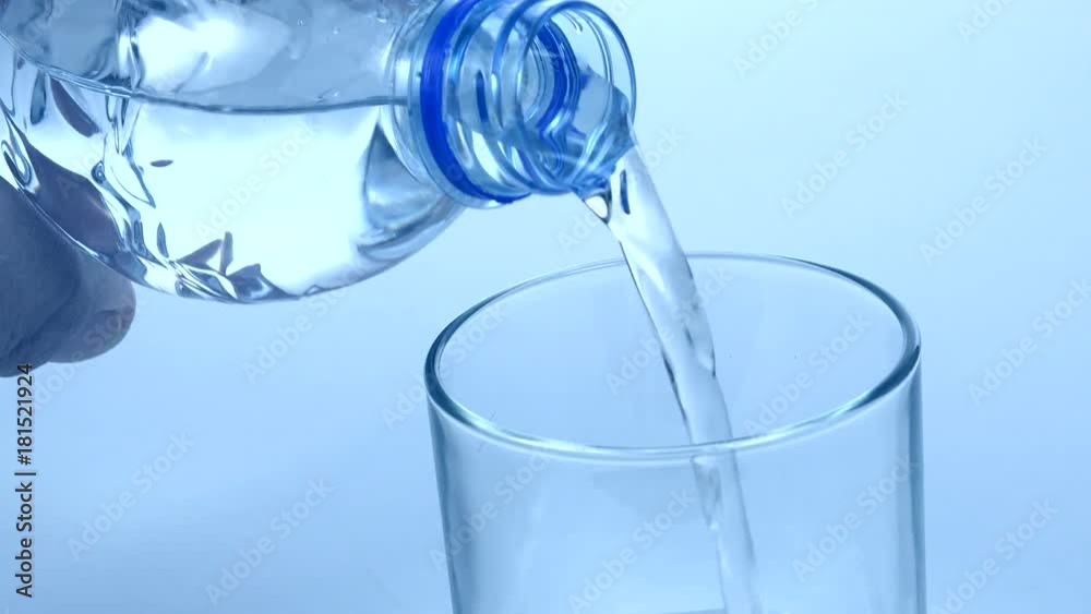 Hand holding drinking water bottle pouring water into glass on blue background Hand holding drinking water bottle pouring water into glass on blue background