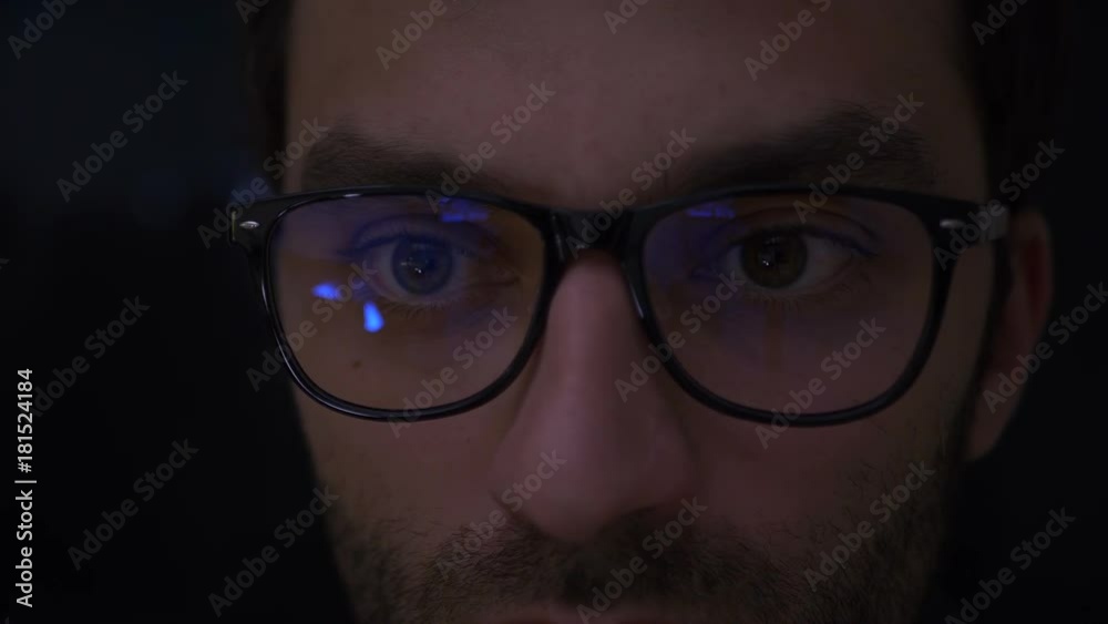 Portrait Man earns bitcoins on his bitcoin farm. Closeup shot of boy in glasses surfing internet at night. Close up of young man reading his tablet in the dark. Black background in focus. Slow Motion