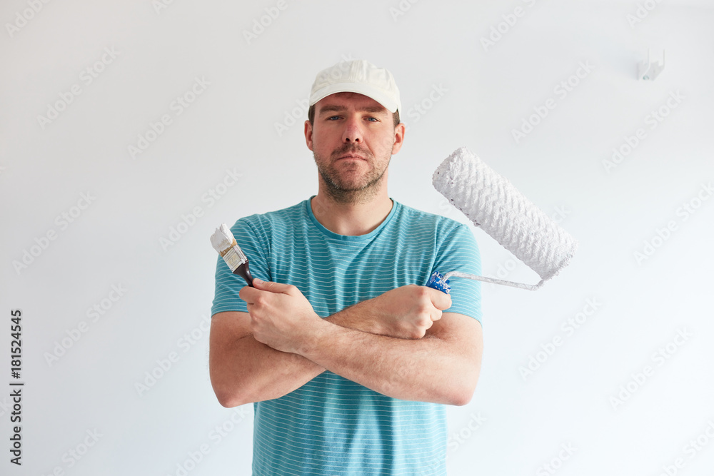 Young man holding a brush and a roller in front of him Young man holding a brush and a roller in front of him