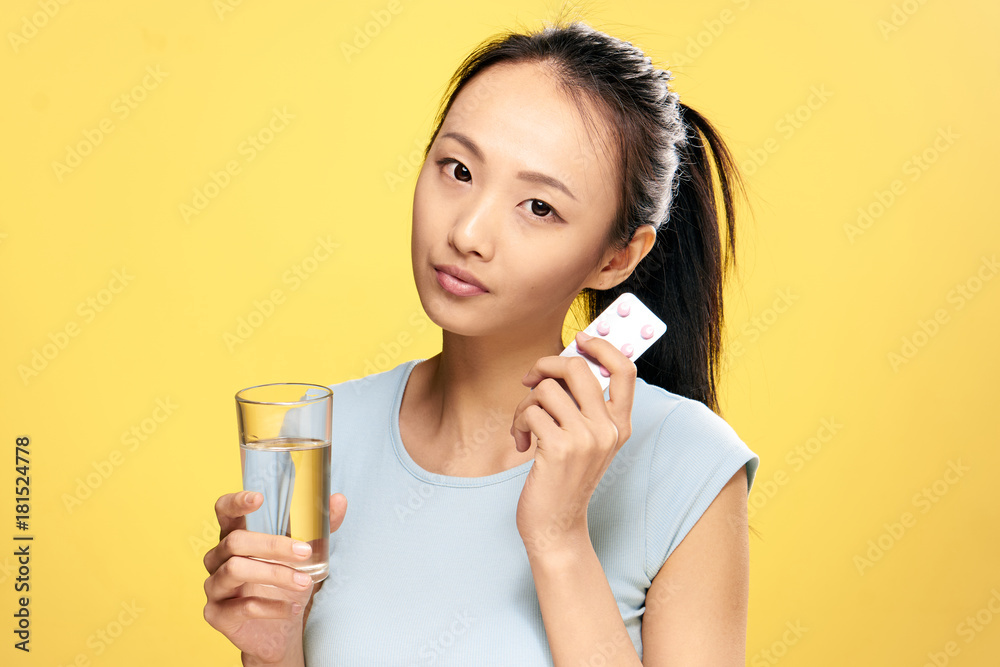 Asian, pill, glass of water, girl holding pills, health, illness, treatment, girl on yellow background Asian, pill, glass of water, girl holding pills, health, illness, treatment, girl on yellow background