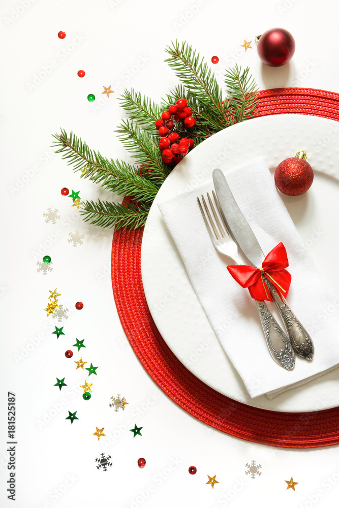 Christmas table setting with white dishware, silverware and red decorations on white background. Top view. Christmas table setting with white dishware, silverware and red decorations on white background. Top view.