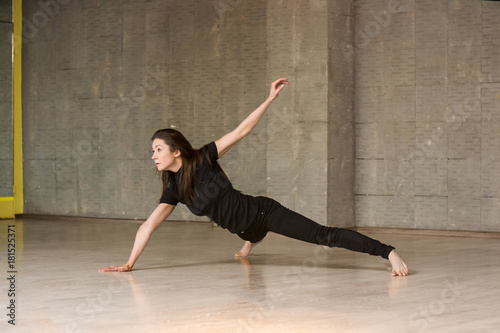 Young dancer practicing gymnastic element. Pretty woman in black suit dancing modern dance on studio background.