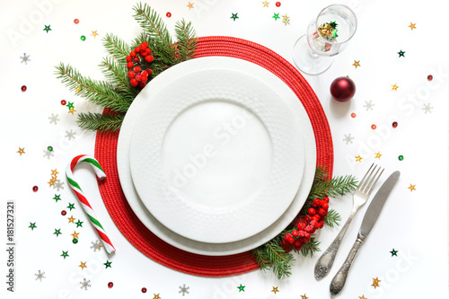 Christmas table setting with white dishware, silverware and red decorations on white background. Top view.