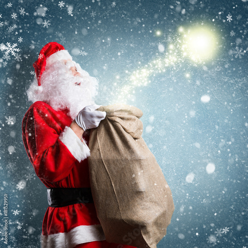 Weihnachtsmann mit Geschenkesack und Magie vor Winterhintergrund #181529951