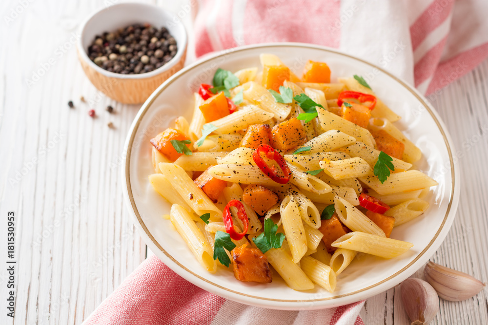 Penne pasta with pumpkin, chilli and parsley in plate on white wooden background Penne pasta with pumpkin, chilli and parsley in plate on white wooden background