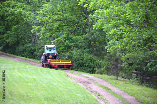 Farm Tractor Pulling Hay Disc Across Dirt Path on Country Farm