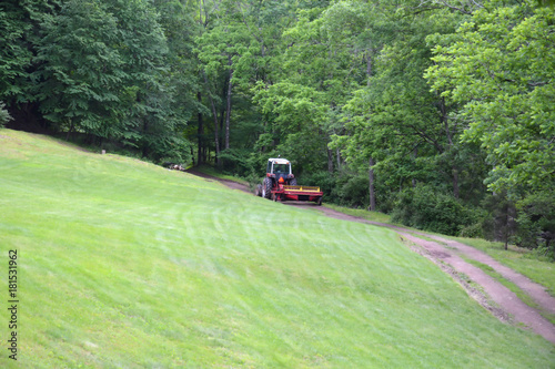 Farm Tractor Pulling Hay Disc Across Dirt Path on Country Farm