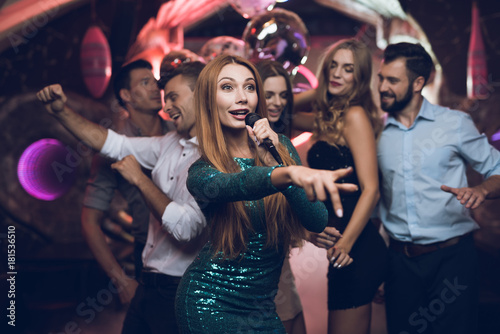 A woman in a green dress is singing songs with her friends at a karaoke club. Her friends have fun on the background.