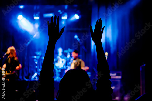 Silhouette of female hands raised at a rock concert in front of the stage with musicians