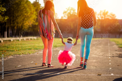 mom and aunt walking with a little girl on a sunny day in the park