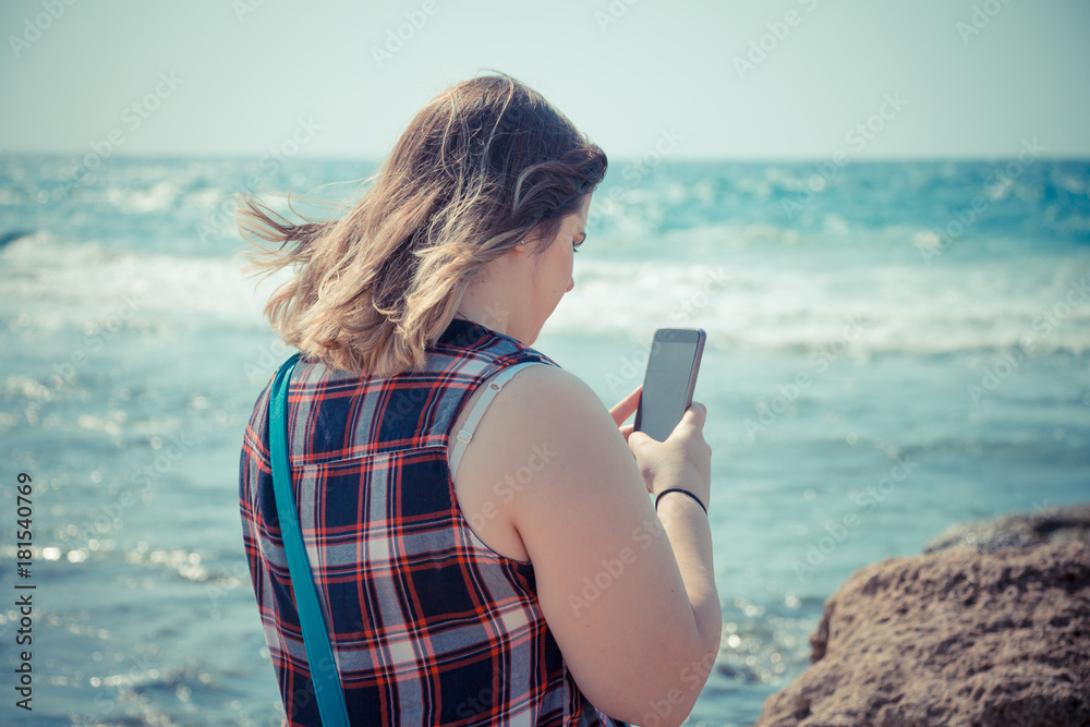 Woman using her smartphone outdoors at the beach near the sea