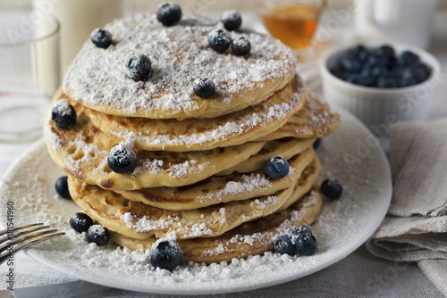 Tasty breakfast of pancakes with blueberries, powdered sugar, milk and honey in a white plate