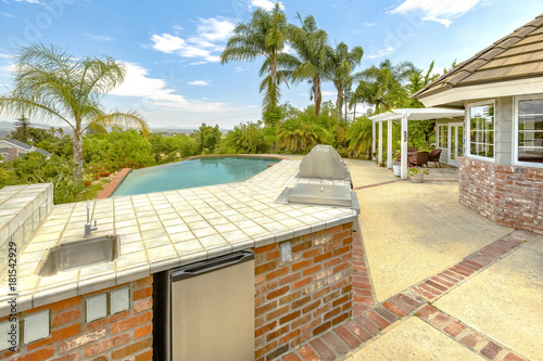 Day shot of a wonder California home with a large pool and counter space for a barbeque on a bright sunny day with puffy clouds