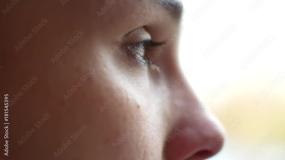 A girl in depression sits near a window. She wipes tears from her eyes, close-up A girl in depression sits near a window. She wipes tears from her eyes, close-up