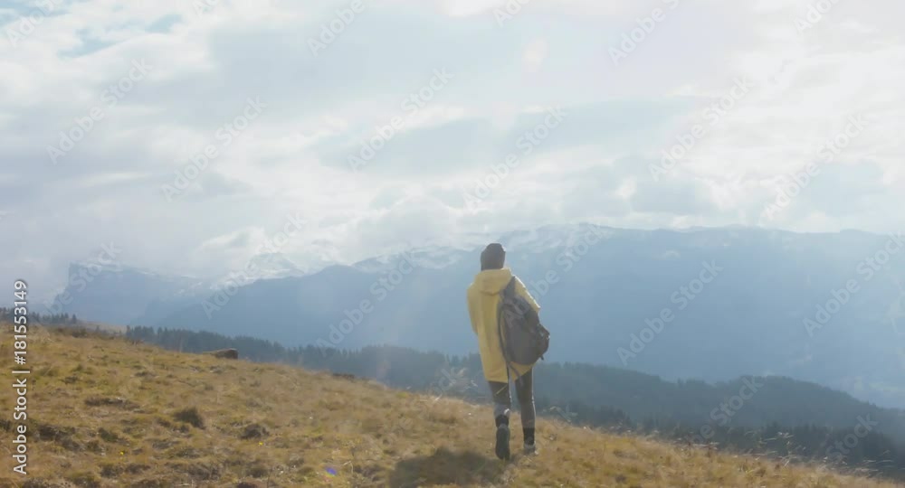 CU TO MED CRANE SHOT Caucasian female hiker in yellow raincoat wearing backpack halts on a scenic spot on the mountain top. 4K UHD RAW 60 FPS SLO MO CU TO MED CRANE SHOT Caucasian female hiker in yellow raincoat wearing backpack halts on a scenic spot on the mountain top. 4K UHD RAW 60 FPS SLO MO
