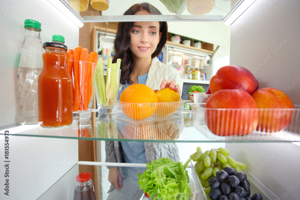 Portrait of female standing near open fridge full of healthy food, vegetables and fruits. Portrait of female Portrait of female standing near open fridge full of healthy food, vegetables and fruits. Portrait of female