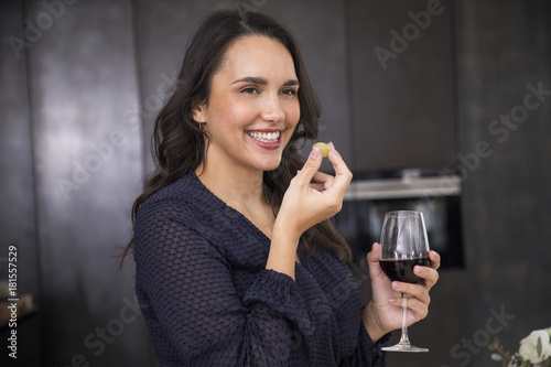 Mujer sonriente y elegante come uvas y bebe vino tinto