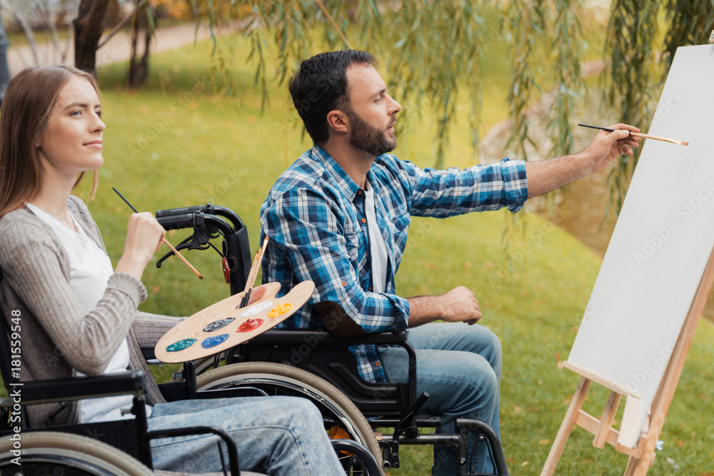A man and a woman with invalids in wheelchairs draw together a picture in the park. A man and a woman with invalids in wheelchairs draw together a picture in the park.