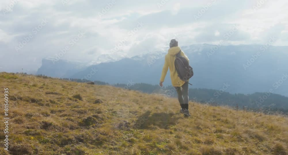 CU TO MED CRANE SHOT Caucasian female hiker in yellow raincoat wearing backpack halts on a scenic spot on the mountain top. 4K UHD RAW 60 FPS SLO MO CU TO MED CRANE SHOT Caucasian female hiker in yellow raincoat wearing backpack halts on a scenic spot on the mountain top. 4K UHD RAW 60 FPS SLO MO