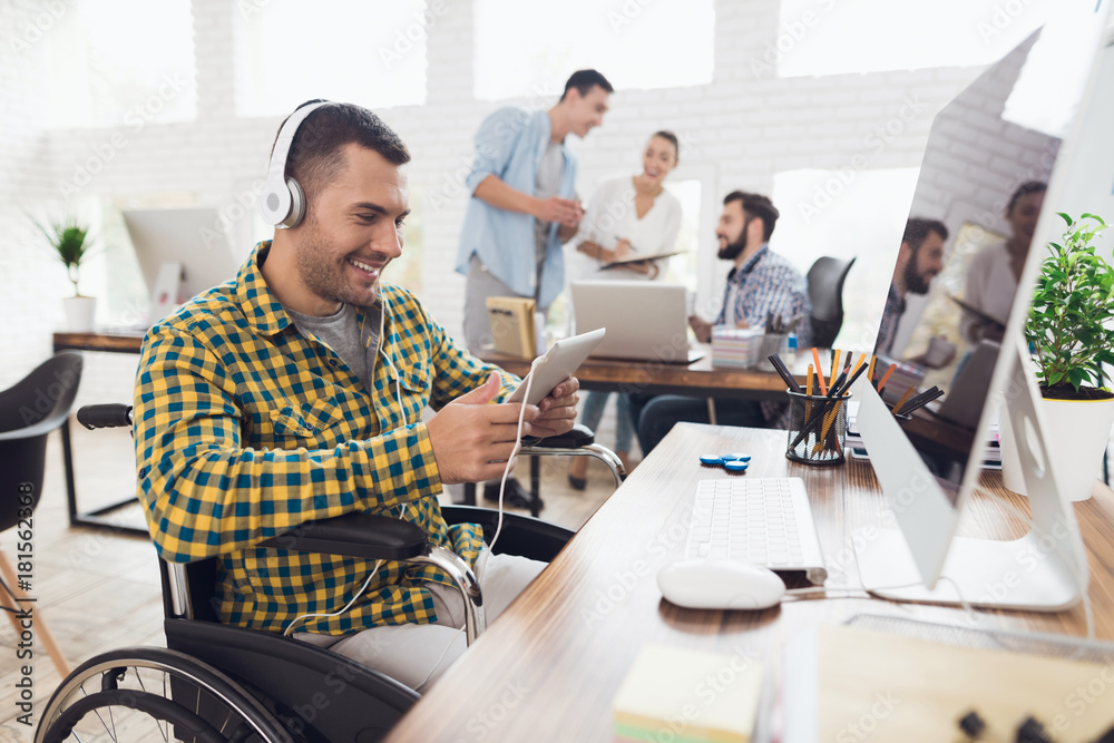 Obraz premium A man in a wheelchair works with a tablet and listens to music on headphones.