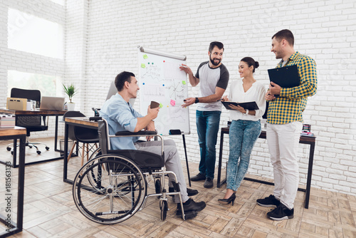 Office workers and man in a wheelchair discussing business moments while working in a modern office.