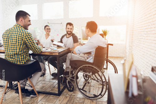 A man in a wheelchair communicates cheerfully with employees of the office during a business meeting. photo