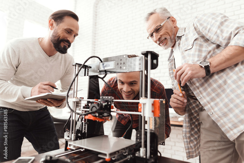 Three men set up a self-made 3d printer to print the form. They are preparing to launch the device for the first time.