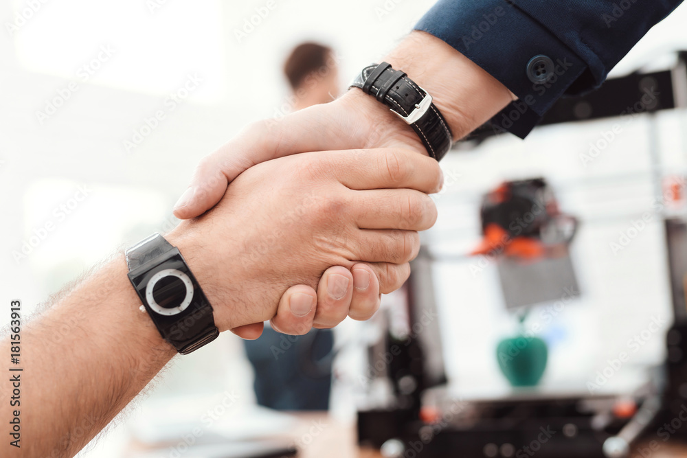 Two men shake hands in the engineering laboratory. Behind them is a 3d printer. Two men shake hands in the engineering laboratory. Behind them is a 3d printer.