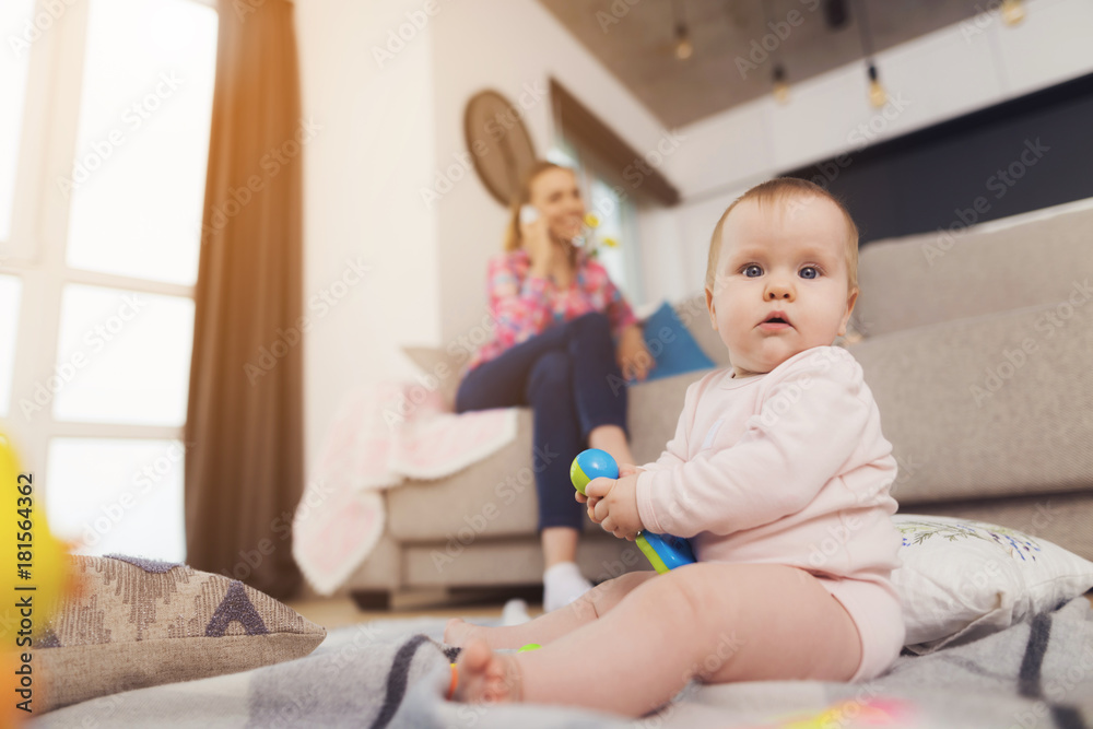 A small child sits on the floor and plays toys. Mum reenka is sitting next to on the couch. A small child sits on the floor and plays toys. Mum reenka is sitting next to on the couch.
