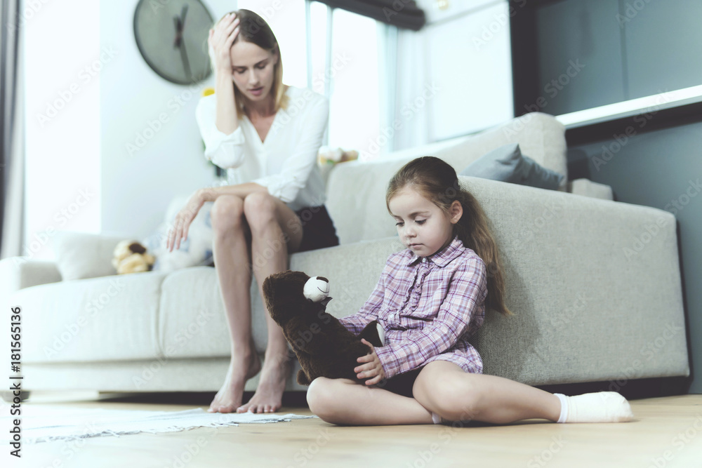 The woman is talking to a small offended girl, who sits next to the sofa and holds a toy in her hands. The woman is talking to a small offended girl, who sits next to the sofa and holds a toy in her hands.