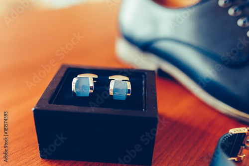 Set of groom cufflinks in blue box on the background of an expensive watch, classic leather shoes, mens accessories of a businessman on a wooden table. Closeup. Vintage tonted photo. photo