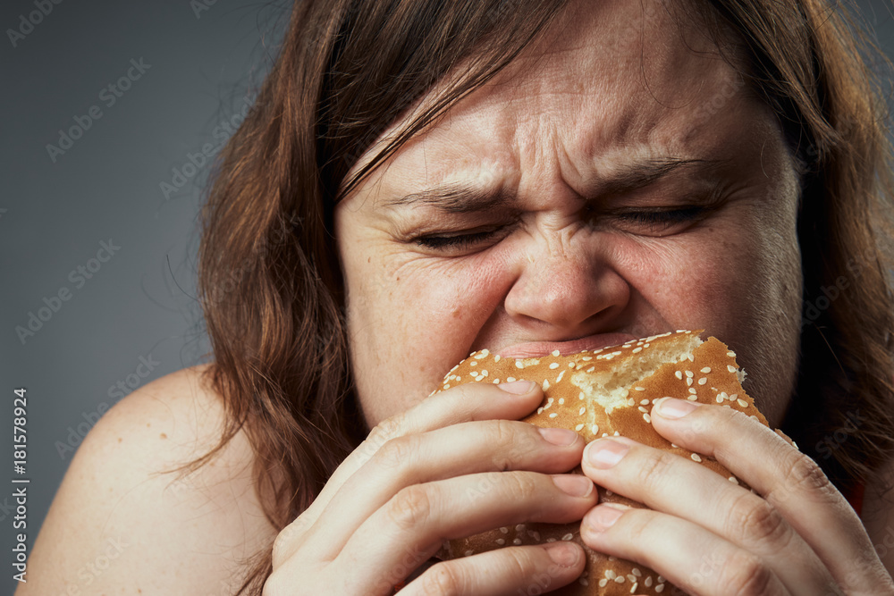 Diet, fast food, woman on a gray background eating a hamburger Diet, fast food, woman on a gray background eating a hamburger
