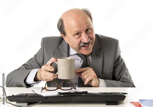 friendly 60s bald senior business man holding coffee cup drinking happy having breakfast at office computer desk smiling