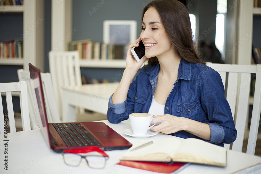 Beautiful smiling women at the table and working at a laptop and speaking on smartphone. Co working zone. Beautiful smiling women at the table and working at a laptop and speaking on smartphone. Co working zone.