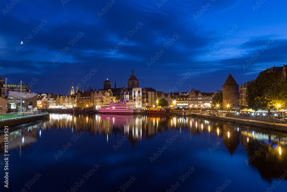 Scenic view of the Motlawa River and lit old buildings on the Long Bridge waterfront at the Main Town (Old Town) in Gdansk, Poland, in the evening. Copy space.