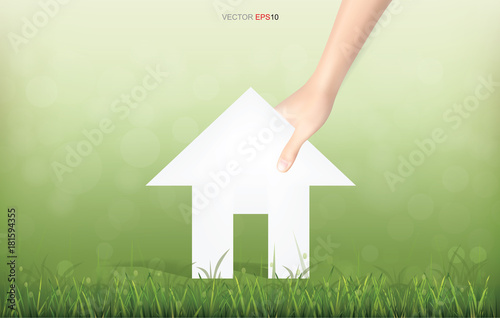 Hand pick a paper house on green yard area. Conceptual image of real estate idea. Vector illustration.