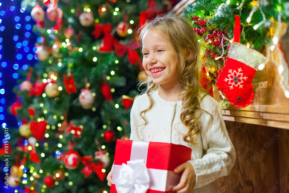 Little girl sitting by the tree holding a Christmas gift a lot o