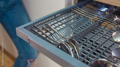 Putting dirty small forks into rack for cuterly of the modern dishwasher and push it inside. photo