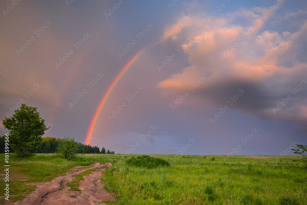 Road to the field. Rainbow in summer. Road leaving into the distance. Beautiful clouds in the sky.