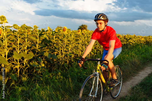 The cyclist in red blue form rides along fields of sunflowers. In background a beautiful blue sky.